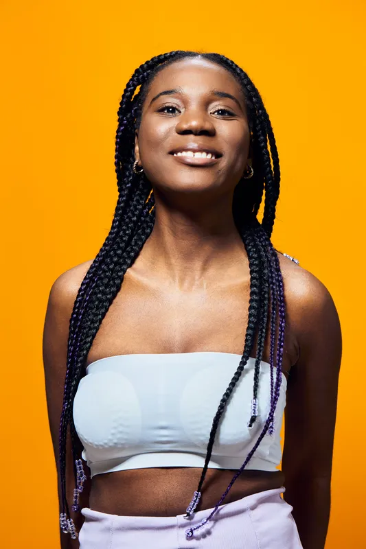 Smiling young woman with braided hair wearing a light top against a vibrant orange background, conveying confidence and joy, ideal for lifestyle and beauty themes