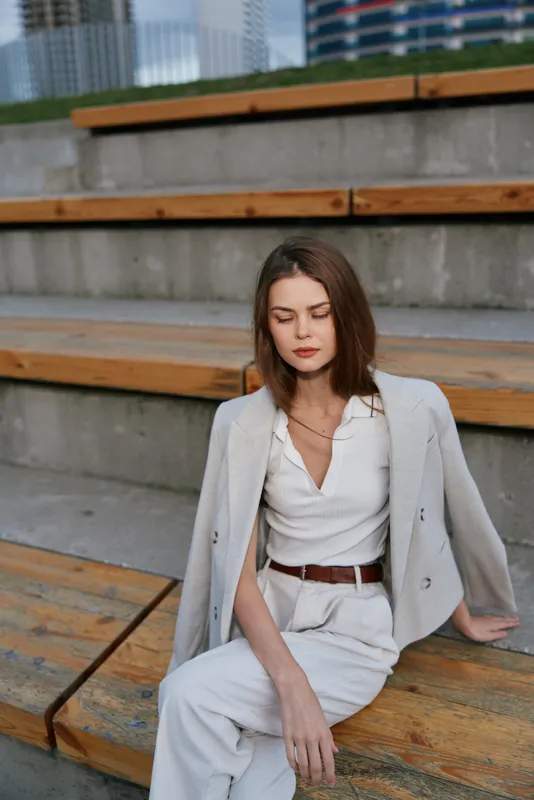 Stylish woman in a business suit sitting outdoors, conveying confidence and professionalism against a modern urban backdrop.