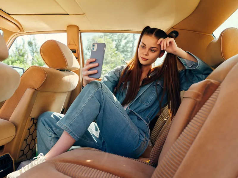Young woman in denim outfit sitting in car, taking a selfie in a relaxed pose, showcasing casual style and summer vibes.