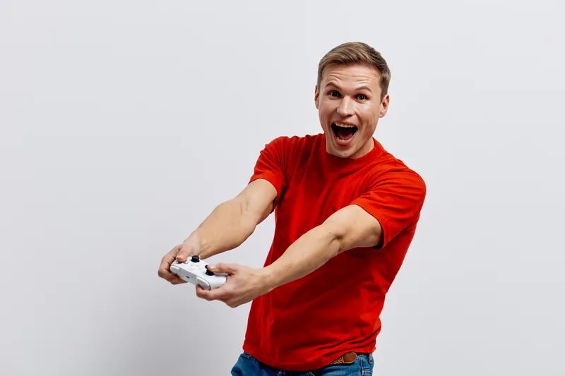 excited smiling young caucasian man wear red t-shirt holding gamepad play video game isolated on plain white background digital detox concept gaming joy