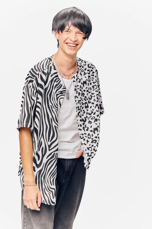 smiling man wearing black and white animal print shirt standing relaxed against white background with casual expression and modern hairstyle, youthful atmosphere