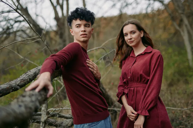 A candid portrait of two young adults in a natural woodland setting, showing authenticity and honest connection through relaxed poses, natural light, textured clothing and subtle emotion.