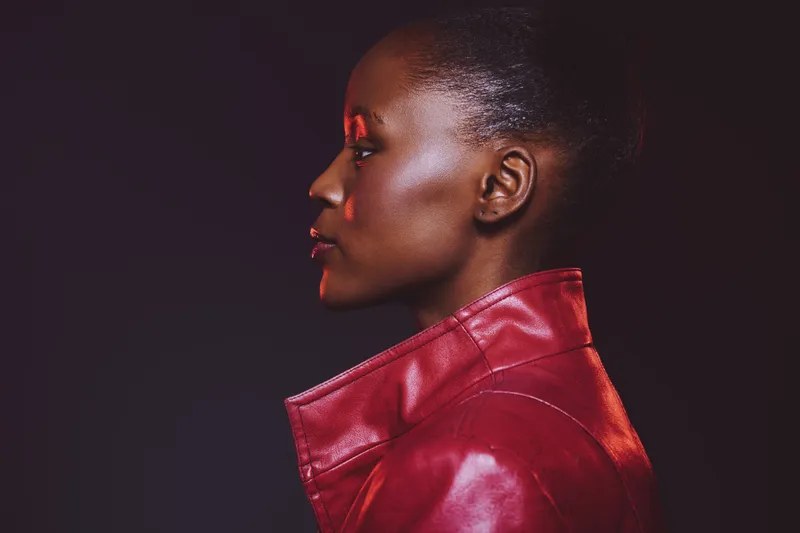 Profile of a confident black African woman with dark skin wearing a red leather jacket against a dark background. Concept of fashion, beauty, style, and empowerment in portrait photography.