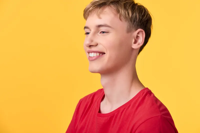 Smiling young man in a red shirt against a vibrant yellow background, casual pose communicates friendly confidence, bright color contrast and positive mood for lifestyle, web and advertising use
