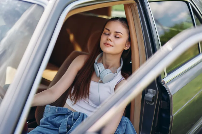 Young woman relaxing in a car, wearing headphones, enjoying the moment in a natural outdoor setting, conveying a sense of peace and tranquility.