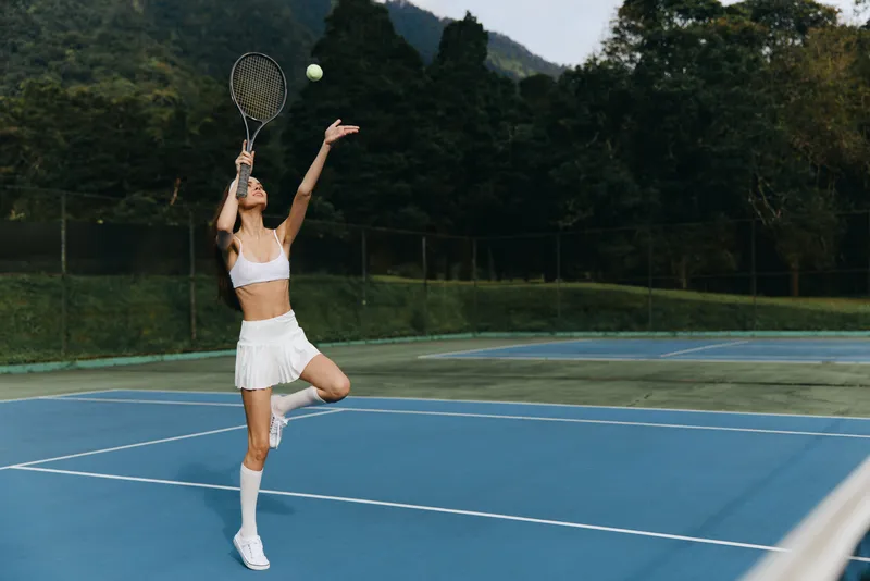 Young athletic woman preparing to serve tennis ball on a sunny day, wearing sporty outfit, showcasing focus and determination on the court