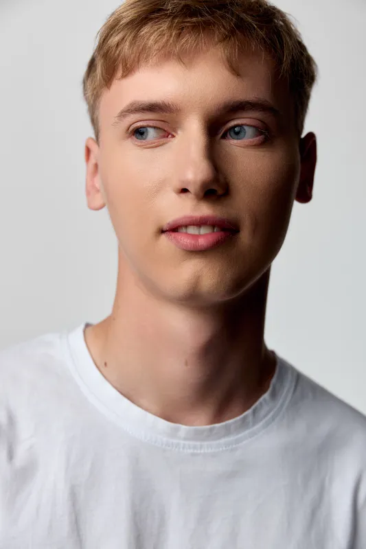 Young man, face with calm expression, wearing white tshirt, soft lighting, neutral background, casual style, looking away, simple studio setup for lifestyle or fashion use