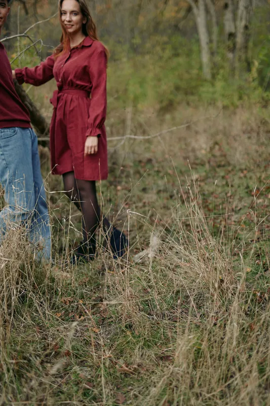 Candid portrait of a woman in a red dress standing in a wild meadow, conveying an authentic and trustworthy moment of quiet connection, natural presence and relaxed confident body language.