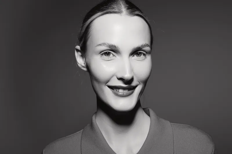 Smiling caucasian woman with pale skin looks at camera in black and white portrait. Studio lighting highlights facial features and natural expression of confidence.