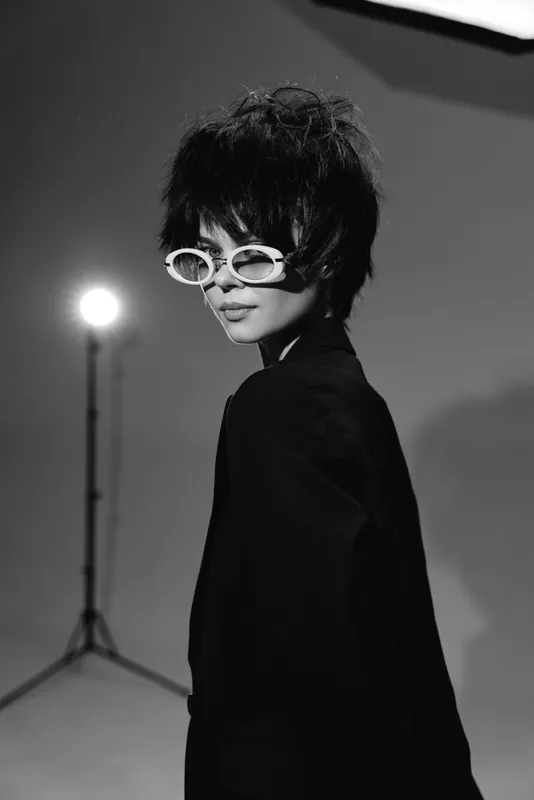 Black and white stylish woman wearing unique sunglasses posing in studio with dramatic lighting and moody atmosphere