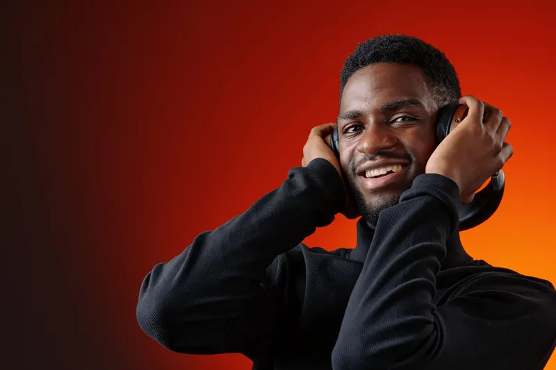 Happy young man enjoying music with headphones on a gradient orange background, expressing joy and relaxation, perfect for music and lifestyle themes