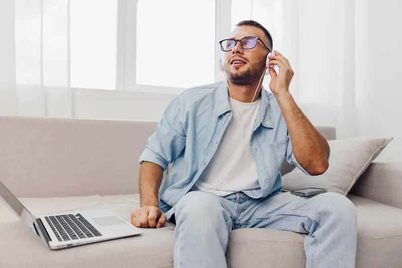 Engaging man enjoying music while working on a laptop, wearing stylish glasses. Bright indoor setting fosters a creative and relaxed atmosphere.