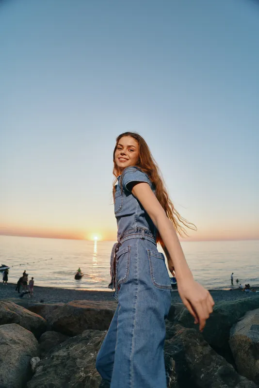 Lifestyle woman in modern boho-western denim street style enjoys sunset beach with film color tones and relaxed natural mood, smiling and carefree outdoors.