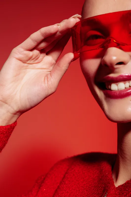Close-up of smiling woman wearing red sunglasses and red sweater on red background. Bright fashion portrait with vibrant colors and happy mood. Concept of style and confidence.