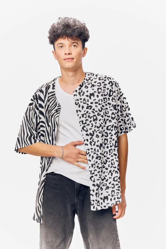 young man wearing a mixed animal print shirt and casual jeans stands against a white background with a neutral expression and relaxed posture, modern style