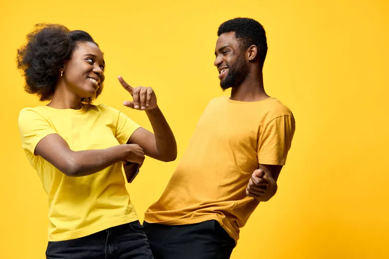 Happy young African couple dancing joyfully in yellow shirts against a bright yellow background, capturing a playful moment of connection and fun