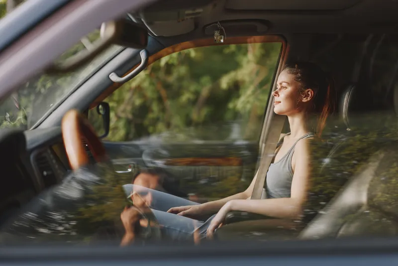 Thoughtful young woman in a car, enjoying nature, reflecting on life, tranquility amidst greenery, stylish and casual attire, serene and peaceful emotion