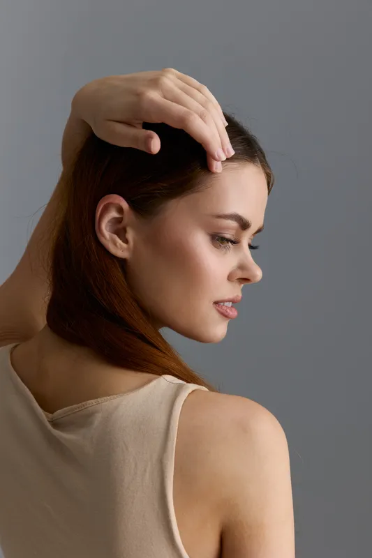 Beauty woman with red hair posing in beige top against gray background, natural makeup, serene expression, soft lighting highlighting smooth skin and elegant look.