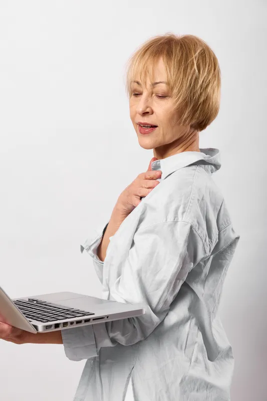 Woman, shoulder, pain, laptop, workplace, health, stress, discomfort shown by worried adult woman holding her aching shoulder, working at desk with computer, isolated on light background