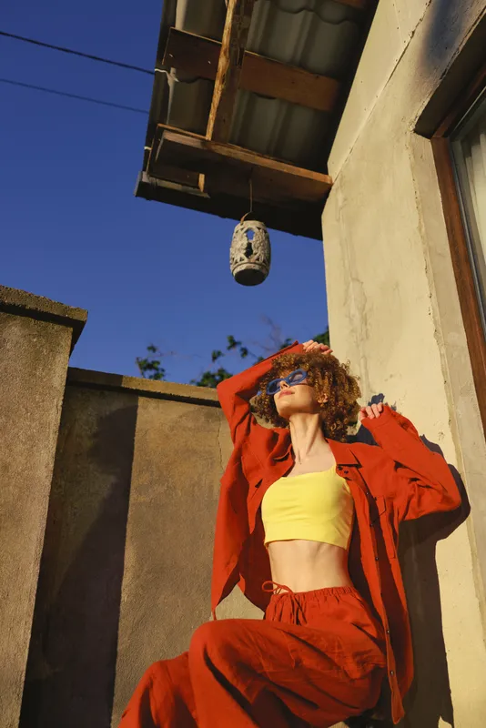 Smiling woman lifestyle fashion outdoor street style, confident pose in bold red suit and yellow top. Sunny urban backdrop, candid moment reflecting empowerment and self expression