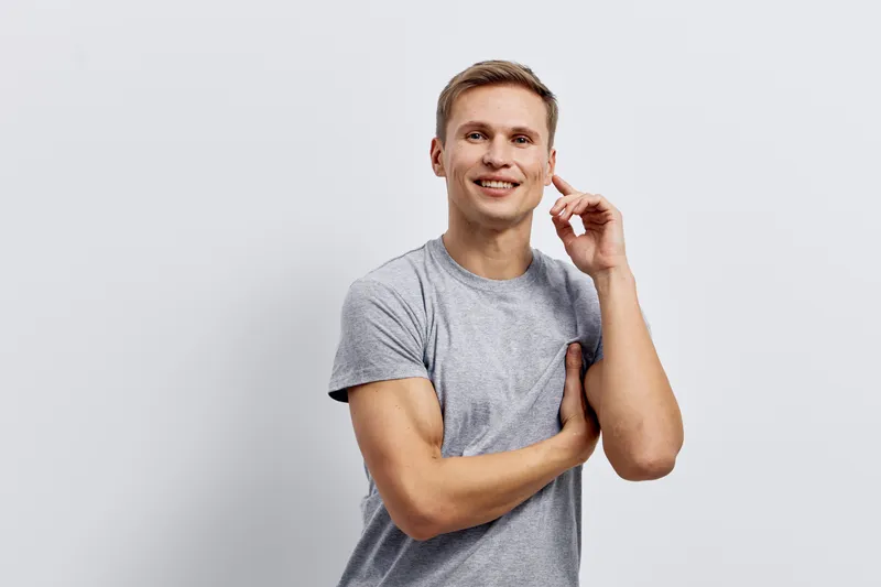 smiling man wearing gray t-shirt touching ear look camera isolated on light background cybersecurity concept technology communication portrait