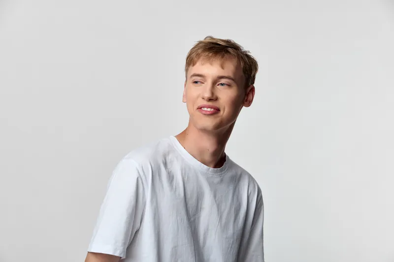 Smiling young man in a casual white tshirt stands against a neutral studio backdrop, conveying relaxed confidence, modern style and approachable charm for lifestyle or fashion projects