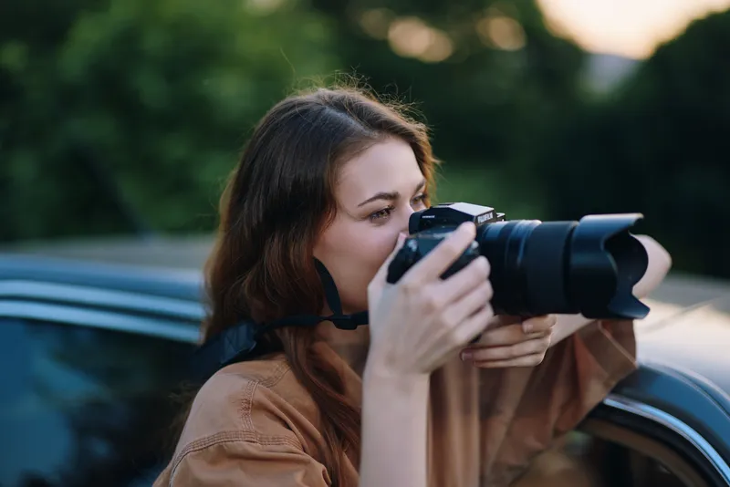 A young woman photographer capturing outdoor images with a DSLR camera, wearing a stylish brown shirt, showcasing creativity and passion for photography.