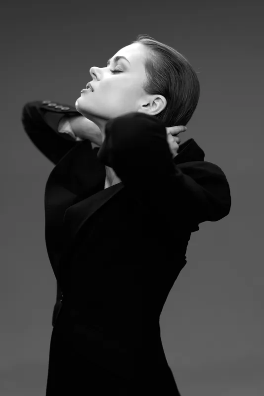 Elegant woman in black blazer posing with eyes closed in a black and white portrait, showcasing confidence and sophistication.