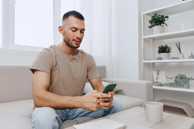Engaged man using smartphone in a stylish living room, showcasing modern lifestyle and technology trends, reflecting comfort and connection, with a touch of minimalism.