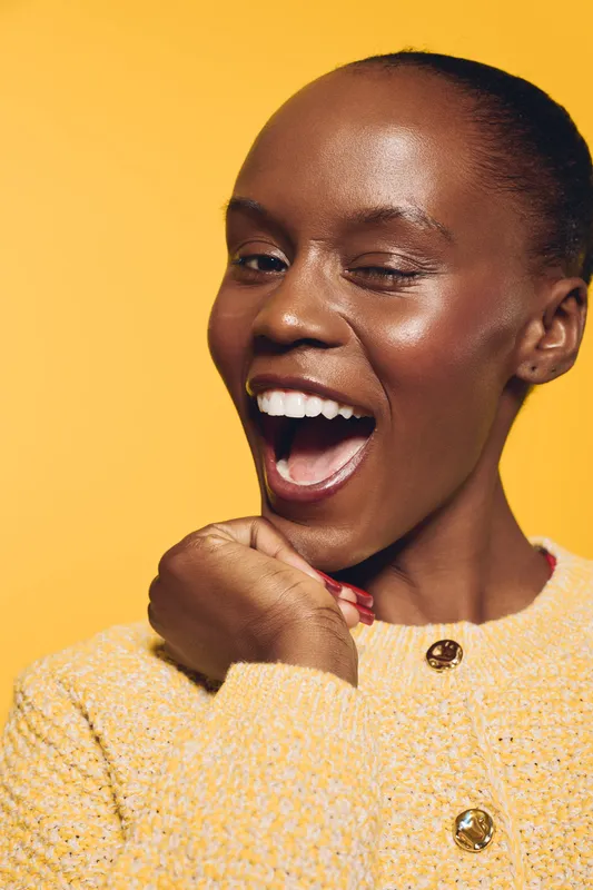 Happy African woman with dark skin and short hair wearing yellow sweater poses with open mouth and bright smile on yellow background. Concept for joy, beauty, and positive emotions.