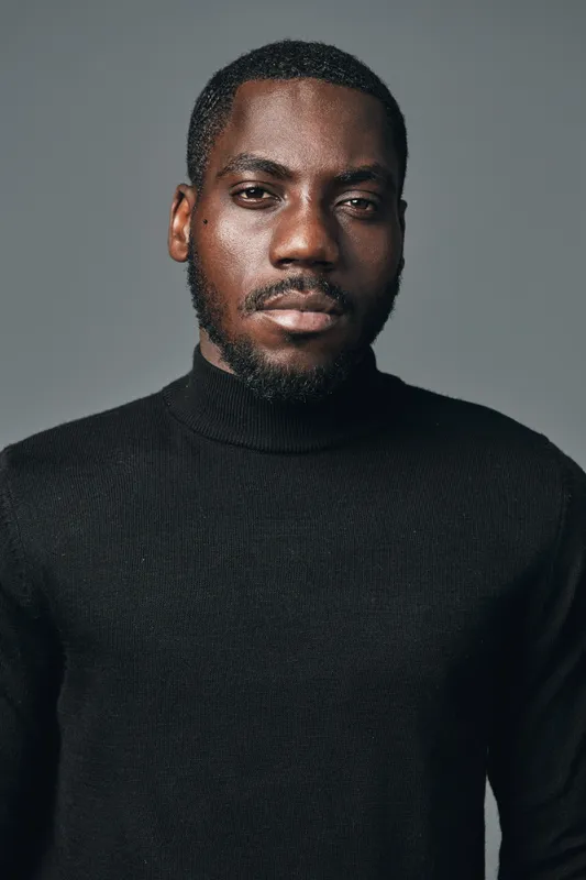 African American man with dark skin wearing black turtleneck sweater looking confidently at camera in creative visual designer style portrait with neutral background.