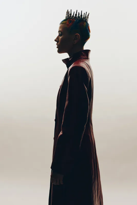 Creative woman with unique crown hairstyle and red leather coat in profile against white background, showcasing alternative fashion and self-expression.