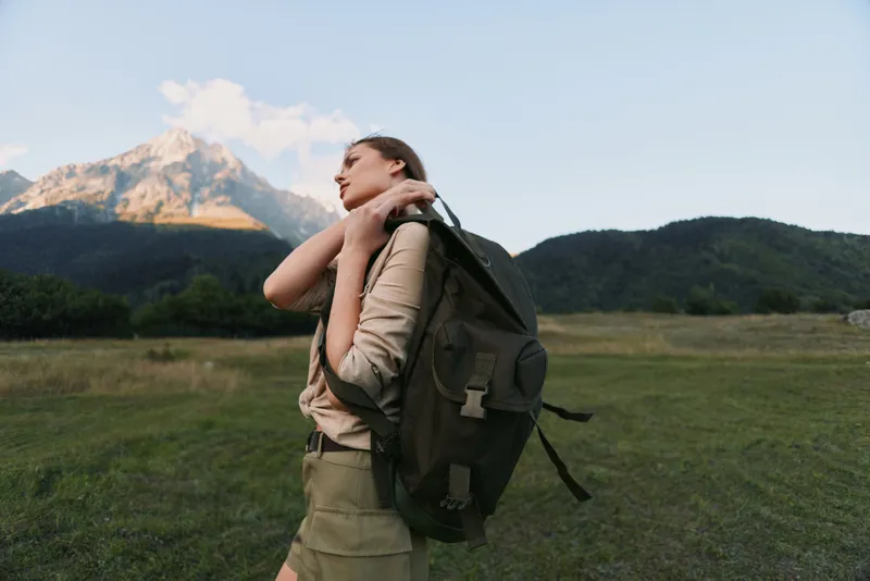 A young woman with a backpack walks across a meadow toward distant mountains, feeling free, focused, curious, and ready for adventure.