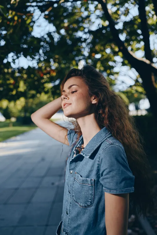 lifestyle woman in modern boho-western denim street style enjoys sunlight, natural setting, relaxed mood, and film color tones in urban outdoor environment