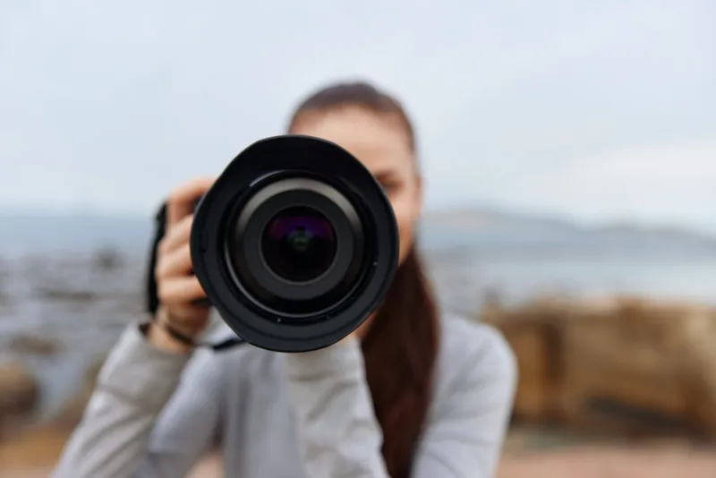 Young woman photographer focusing camera at the beach, showcasing passion for photography amidst a serene coastal backdrop