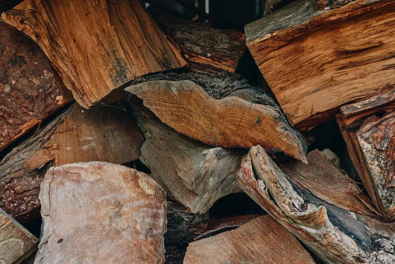 Firewood, stacked logs, hardwood, woodpile, bark texture, split timber arranged for fireplace or camping; rustic outdoor closeup evoking cozy autumn warmth and natural brown tones.