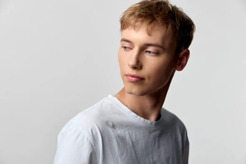 Thoughtful man in a white t shirt gazes to the side in a calm studio setting, casual lifestyle vibe with a clean background and minimalist style