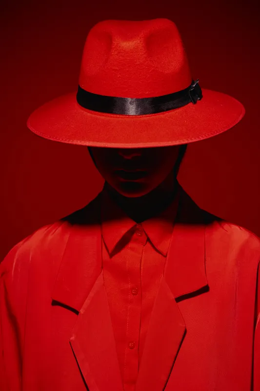 Fashion model wearing a red hat and a matching red outfit posing against a red background. Concept of beauty, creative fashion, and dramatic style in portrait photography.