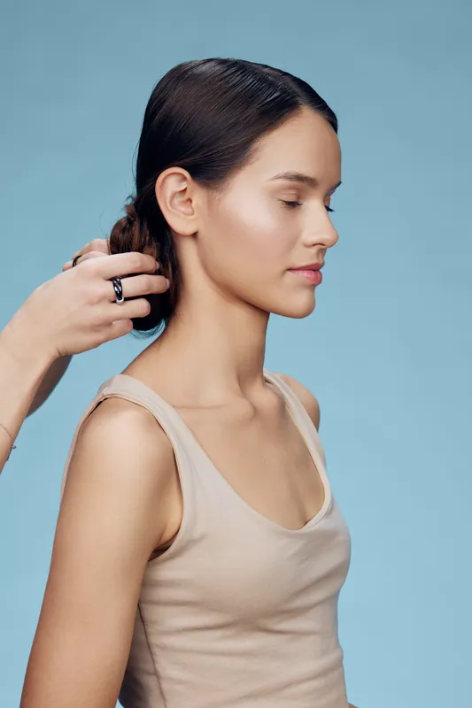Young woman with smooth, sleek hair being styled against a soft blue background, reflecting elegance and beauty concepts in a professional setting