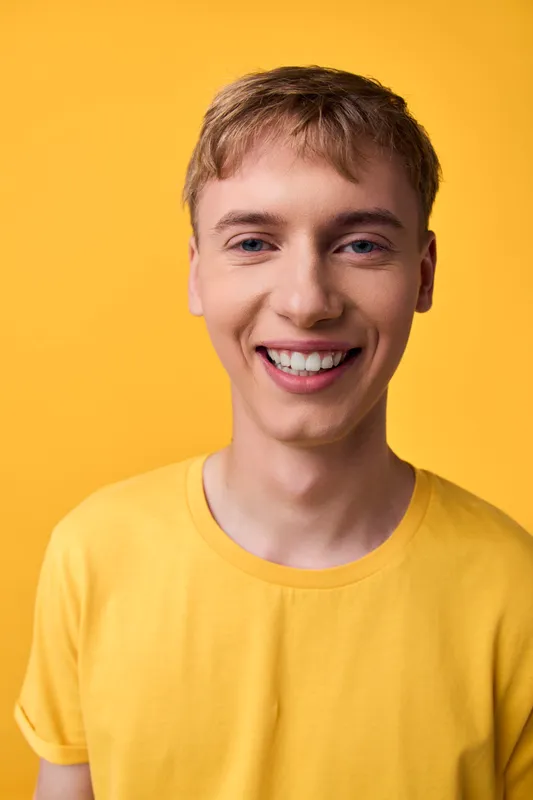 Smiling man in a bright yellow shirt stands against a vivid yellow backdrop, showcasing a cheerful casual look, studio lighting, and positive energy for lifestyle and marketing uses