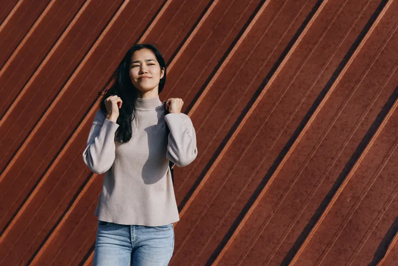 Woman poses against a diagonal wooden wall, wearing a soft knit sweater and denim, casual fashion vibe with a relaxed stance and moody light in a modern urban backdrop