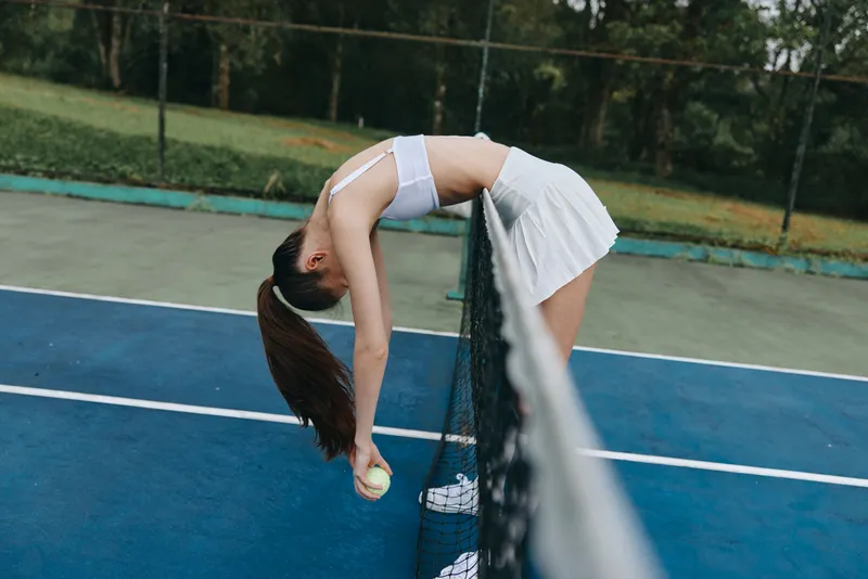 Young female tennis player in a white sports outfit stretching over the net, demonstrating athleticism and determination on a sunny day on a tennis court