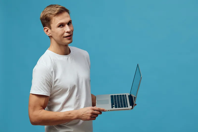 Man holding open laptop computer with thin profile isolated on solid bright blue background studio portrait. Technology, digital device, casual clothing, young adult, professional concept
