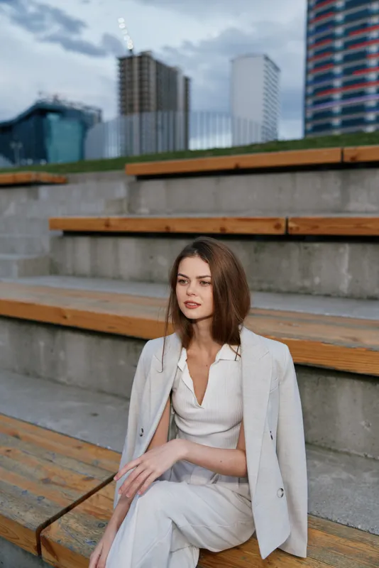 business woman in light suit sitting on urban steps outdoors with modern city background confident professional style