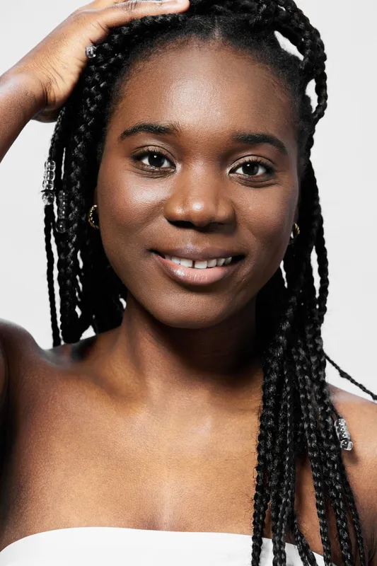 Happy African woman with braided hair, wearing minimal makeup, smiling confidently against a neutral background, showcasing natural beauty and positive emotions