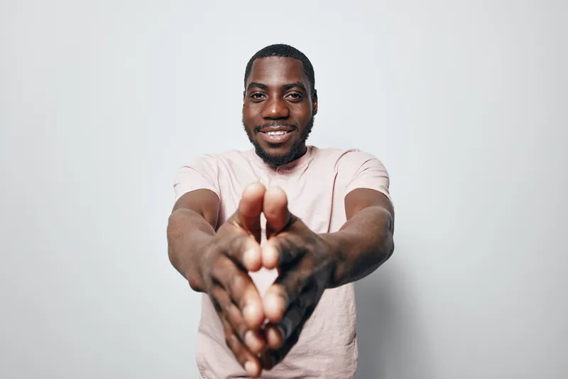 African American man with dark skin smiling and clapping hands wearing casual light pink t shirt on white background. Positive gesture and happy expression.