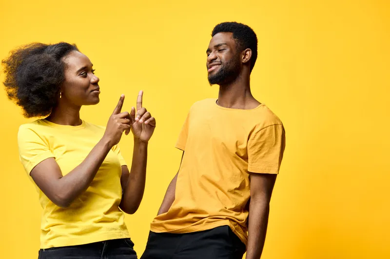 A joyful young African American couple wearing matching yellow shirts, laughing and interacting playfully against a bright yellow background, representing fun and connection
