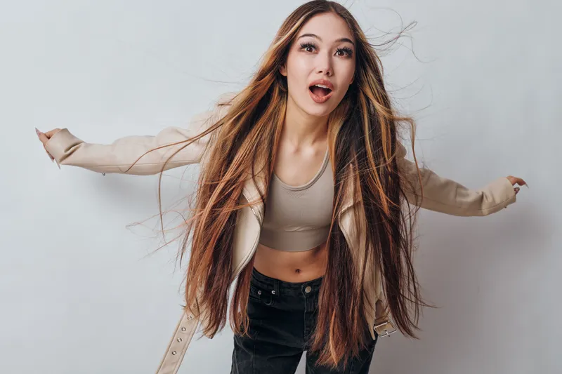 Young woman with long hair and casual clothes posing with surprised facial expression on white background. Fashion portrait of female model showing motion and emotion in studio lighting.