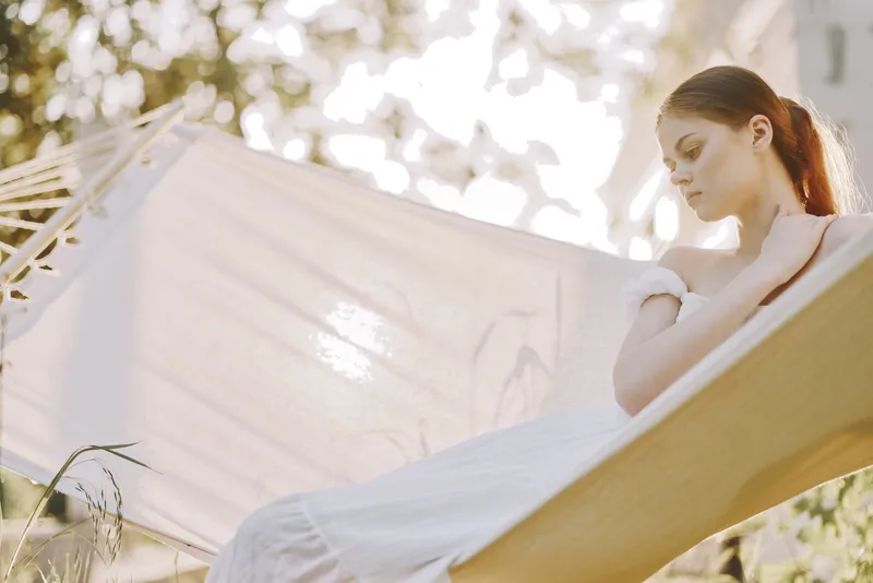 Serene young woman in white dress relaxing in a hammock during sunset, embodying tranquility and nature s beauty with soft natural light