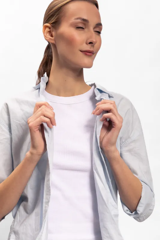 Young woman with closed eyes wears white shirt and light jacket, holding collar. Studio portrait on white background. Concept of calm, confidence, relaxation, fashion, and casual style.